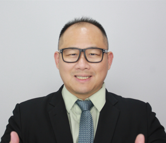 Lim Tau Tat giving a confident thumbs-up in a formal suit and tie